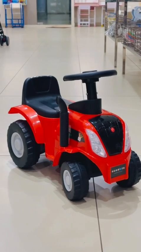 A red Funfizz tractor ride-on with black seat and steering wheel on a showroom floor